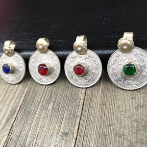 Puede incluir: Cinco colgantes de monedas de plata con piedras de vidrio de diferentes colores en el centro. Las monedas tienen escritura &aacute;rabe alrededor del borde.