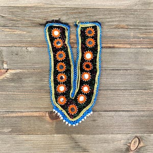 May include: A black and green fabric trim with a V-shape design. The trim is decorated with small round mirrors and orange and blue beads.