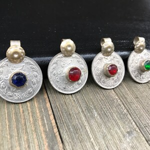 Puede incluir: Cuatro colgantes de moneda de plata con gemas de vidrio de diferentes colores en el centro. Las gemas son azules, rojas, rojas y verdes.