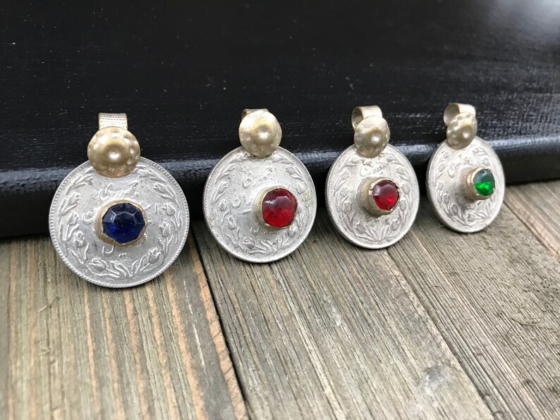 Puede incluir: Cuatro colgantes de moneda de plata con gemas de vidrio de diferentes colores en el centro. Las gemas son azules, rojas, rojas y verdes.