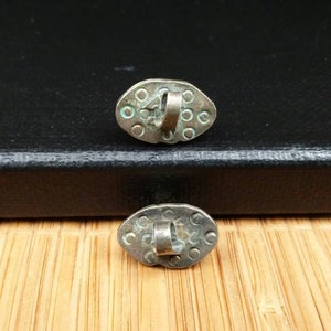 May include: Two silver oval-shaped buttons with a loop on the back. The buttons have a textured surface with small circles.