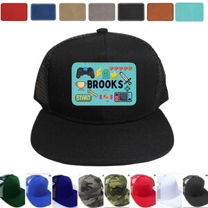 May include: Black trucker hat with a blue and white patch featuring the name "BROOKS" and various gaming icons. The hat is available in a range of colours.