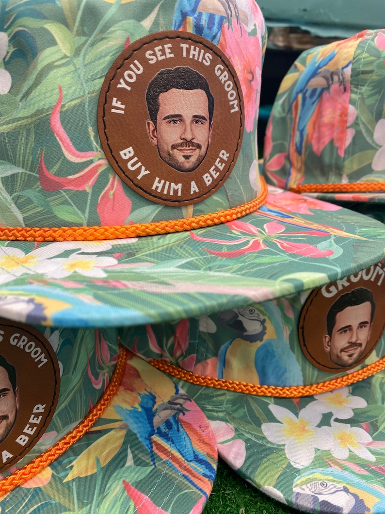 May include: Three tropical print baseball caps with orange trim and a brown leather patch that says "If you see this groom buy him a beer" with a photo of a man on the patch.