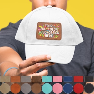 May include: White baseball cap with a brown leather patch that says "YOUR FULL COLOR LOGO/DESIGN HERE" in colorful letters. The patch has a colorful firework design around the text. The cap is being held by a hand.