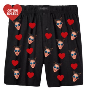 May include: Black cotton boxer shorts with a repeated pattern of red hearts and a face wearing sunglasses. The text "Cotton Boxers" is on a red heart in the top left corner.