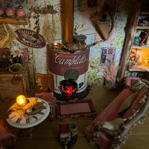 May include: A miniature dollhouse room featuring a red and white Campbell's soup can stove, a pink sofa, a clock, and a small lamp.