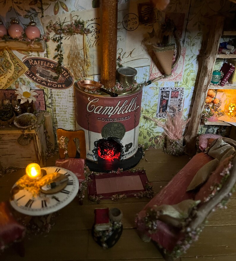 May include: A miniature dollhouse room featuring a red and white Campbell's soup can stove, a pink sofa, a clock, and a small lamp.