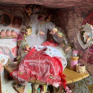 May include: A miniature dollhouse room featuring a red velvet bed with white lace trim and a sheer white curtain. The room is decorated with pink roses, vintage stamps, and a small heart-shaped mirror.