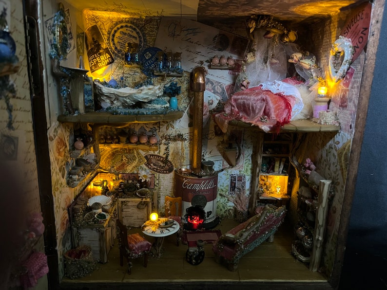 May include: A miniature dollhouse with a detailed interior, featuring a kitchen with a stove, a dining area with a table and chairs, and a bedroom with a bed and a canopy. The dollhouse is decorated with vintage-inspired wallpaper and furniture, and includes small details like a miniature can of Campbell's soup and a miniature lamp.