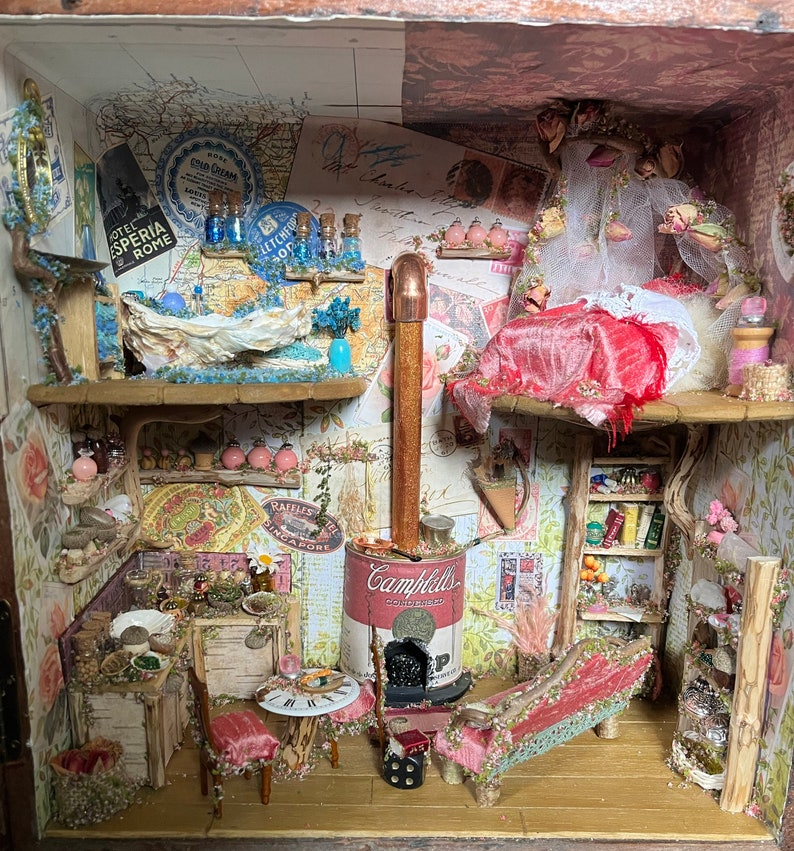 May include: A miniature dollhouse scene featuring a pink and white bed, a fireplace fashioned from a Campbell's soup can, and a tiny kitchen with a wooden table and chairs.