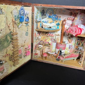 May include: A miniature dollhouse scene featuring a red velvet chaise longue, a wood-burning stove, and a Campbell's soup can. The dollhouse is decorated with vintage wallpaper and floral accents.