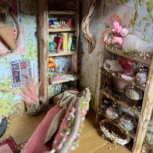 May include: A miniature dollhouse room featuring a wooden bookshelf stocked with books, a red sofa, and a wooden shelf displaying decorative items. The room is adorned with floral wallpaper and a wooden floor.