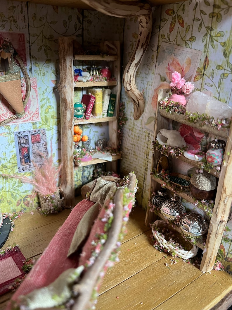 May include: A miniature dollhouse room featuring a wooden bookshelf stocked with books, a red sofa, and a wooden shelf displaying decorative items. The room is adorned with floral wallpaper and a wooden floor.