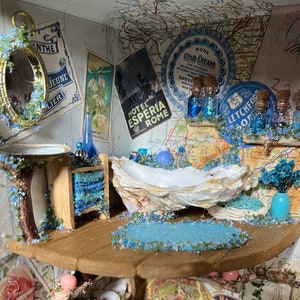 May include: A miniature bathroom scene featuring a seashell bathtub, a wooden vanity with blue towels, and a round mirror. The scene is decorated with blue and white flowers, and a map with the text "Letchford" and "Hotel Esperia Rome".