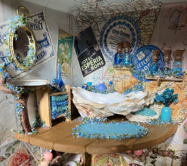 May include: A miniature bathroom scene featuring a seashell bathtub, a wooden vanity with blue towels, and a round mirror. The scene is decorated with blue and white flowers, and a map with the text "Letchford" and "Hotel Esperia Rome".