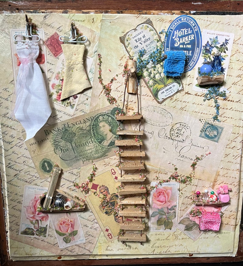 May include: A vintage-inspired collage featuring a miniature wooden ladder, a small white dress, a blue fabric flower, and a variety of paper ephemera, including a Bank of England one pound note, a playing card, and a vintage postcard.