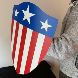 May include: A red, white and blue shield with a star pattern. The shield is made of metal and has a slightly curved shape.