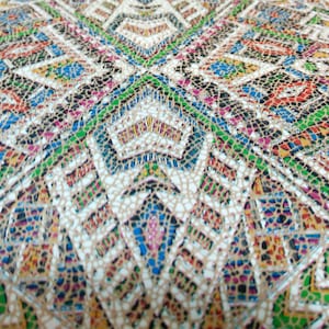 May include: A close-up of a fabric with a colorful geometric pattern. The fabric has a textured surface and is made of a woven material. The pattern is made up of small squares and triangles in shades of red, blue, green, yellow, and white.
