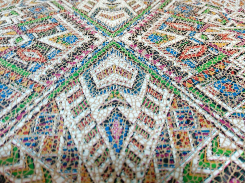 May include: A close-up of a fabric with a colorful geometric pattern. The fabric has a textured surface and is made of a woven material. The pattern is made up of small squares and triangles in shades of red, blue, green, yellow, and white.