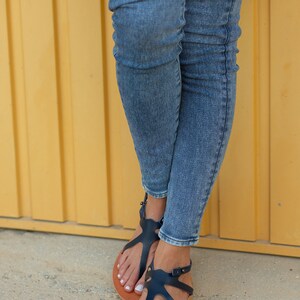May include: A pair of blue denim jeans with a pair of dark blue leather sandals with brown soles.