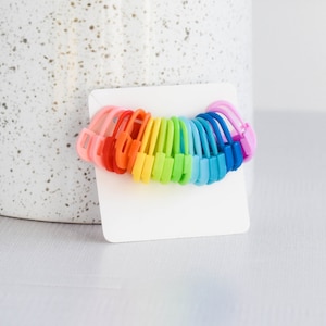 May include: A set of rainbow colored hair ties. The hair ties are arranged in a circle on a white background.