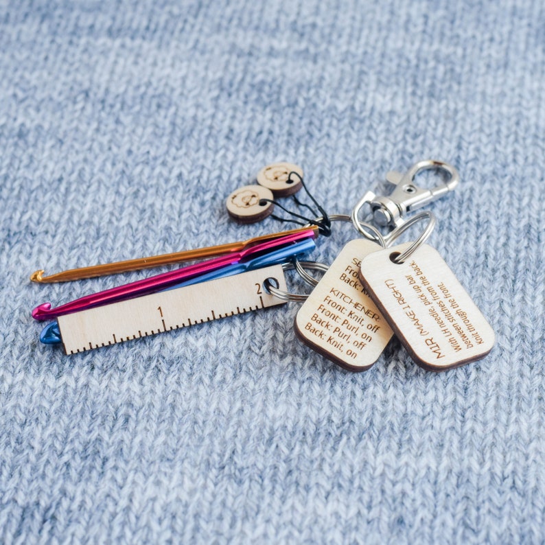 May include: A set of knitting tools including two wooden stitch markers, a wooden ruler, two crochet hooks, and two wooden keychains with instructions for the Kitchener stitch and the "Make 1 Right" stitch.