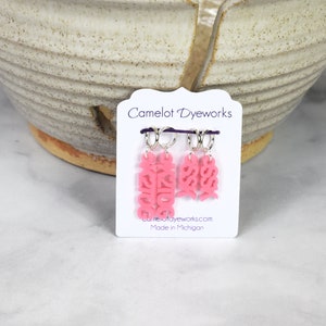 May include: Three pink plastic stitch markers with the words "Kids", "Sis", and "Bro" on them. The markers are attached to silver rings and are displayed on a white card with the text "Camelot Dyeworks" and "Made in Michigan".
