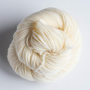 Pu&ograve; includere: Un gomitolo di filato bianco sporco, ben avvolto. Il filato ha un aspetto morbido e una superficie leggermente strutturata, ideale per progetti di maglieria o uncinetto. Il colore neutro lo rende versatile.