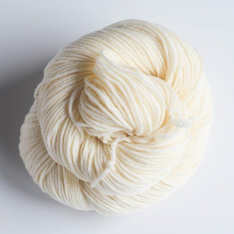 Pu&ograve; includere: Un gomitolo di filato bianco sporco, ben avvolto. Il filato ha un aspetto morbido e una superficie leggermente strutturata, ideale per progetti di maglieria o uncinetto. Il colore neutro lo rende versatile.