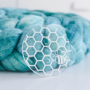 May include: A clear acrylic yarn bowl with a honeycomb pattern and a bee design. The bowl has three holes for yarn.