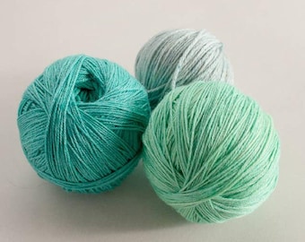 May include: Three balls of yarn in shades of teal, light blue, and mint green. The yarn is tightly wound, showing the texture of the fibers. Ideal for knitting or crochet projects.
