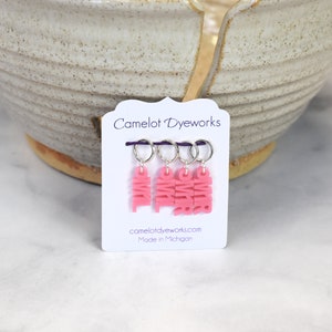May include: Set of four pink stitch markers with the word "PINK" written on each marker. The markers are on a white card with the text "Camelot DyeWorks" and "camelotdyeworks.com Made in Michigan".