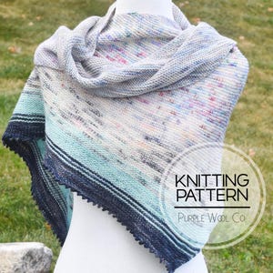 May include: A knitted shawl with a gradient of colors from white to blue, with a black and white border. The shawl is on a white mannequin. The text "Knitting Pattern" and "Purple Wool Co." is on a white circle.