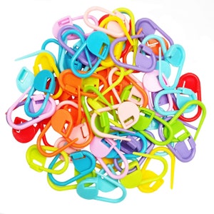 May include: A large pile of colorful plastic stitch markers in various shapes and sizes. The markers are used for knitting and crocheting.