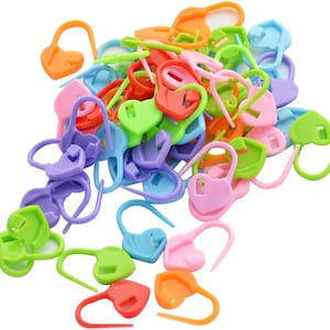May include: A large pile of colorful plastic heart-shaped stitch markers. The markers are in various colors, including pink, purple, blue, green, orange, and red.
