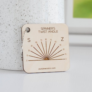 May include: A wooden tool for measuring twist angle, with a scale from 0 to 90 degrees, labeled "Spinner's Twist Angle" and "S" and "Z" at the ends of the scale. The tool has a small metal ring attached to it.