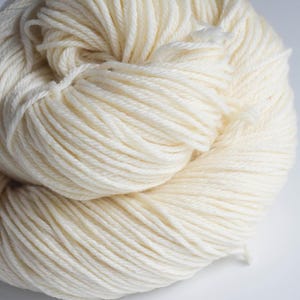 Pu&ograve; includere: Primo piano di un gomitolo di filato bianco sporco. Il filato &egrave; avvolto strettamente, mostrando singoli fili. La trama appare morbida e leggermente sfocata, suggerendo una fibra naturale. Il colore &egrave; un bianco crema caldo, ideale per progetti di maglia o uncinetto.