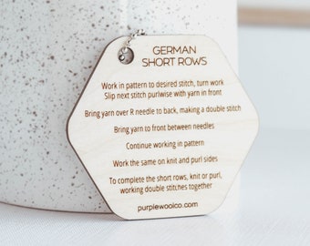 May include: A wooden hexagonal tag with the text "GERMAN SHORT ROWS" and instructions for knitting short rows. The tag is attached to a silver chain.