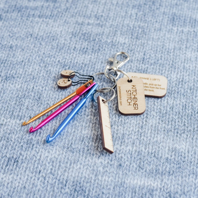 May include: A keychain with a wooden tag that says "KITCHENER STITCH" and "purplerwooluo.com". The keychain also has a wooden ruler, three crochet hooks, and two wooden buttons.