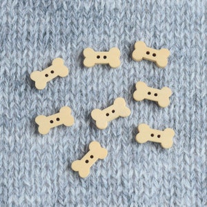 May include: Eight wooden bone-shaped buttons with two holes each, scattered on a gray knitted fabric background.