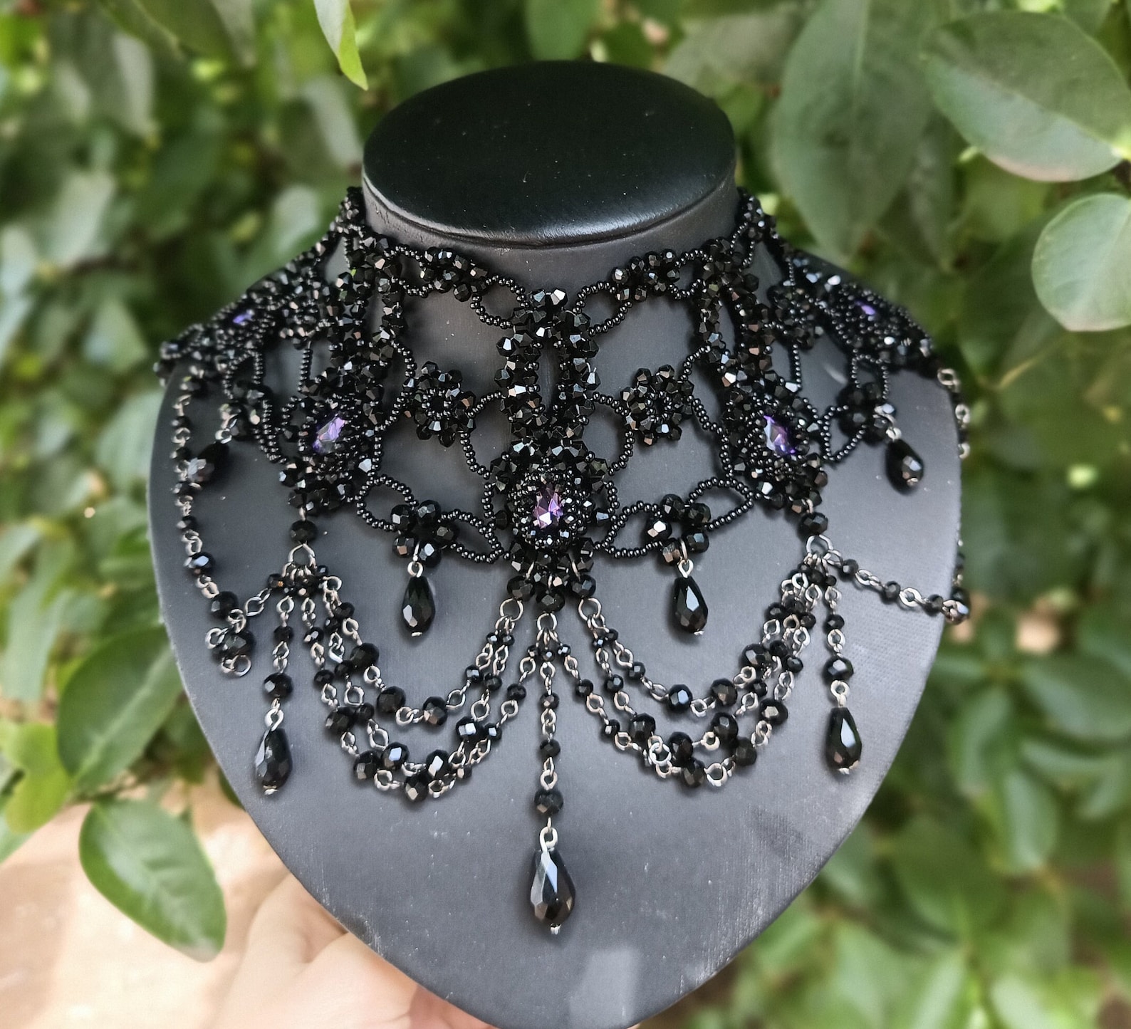 Purple crystal gothic necklace with intricate black beadwork and layered chains on black bust outdoors.