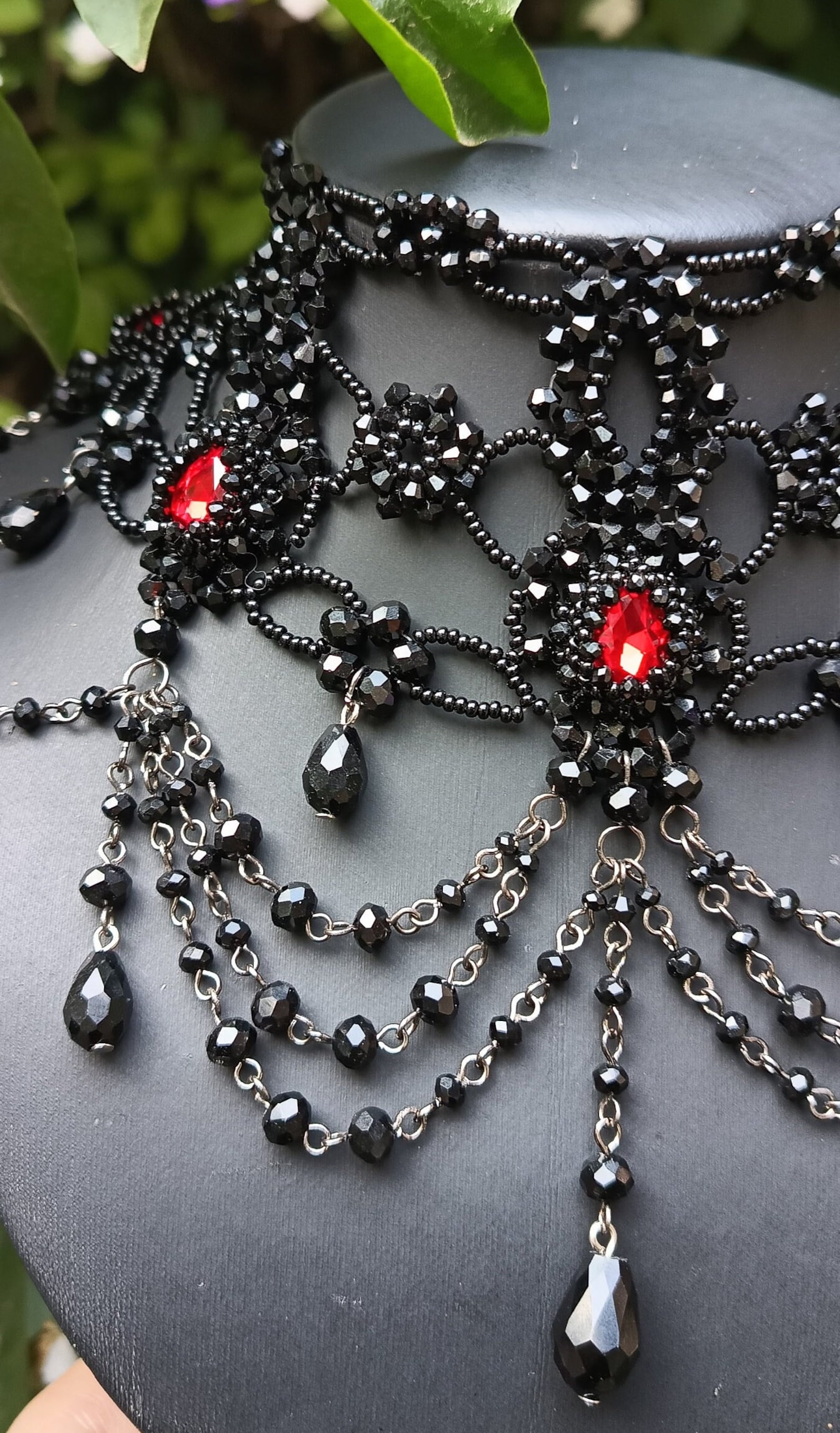 Close-up of red rhinestone gothic necklace with black bead embroidery and cascading black chain drops.