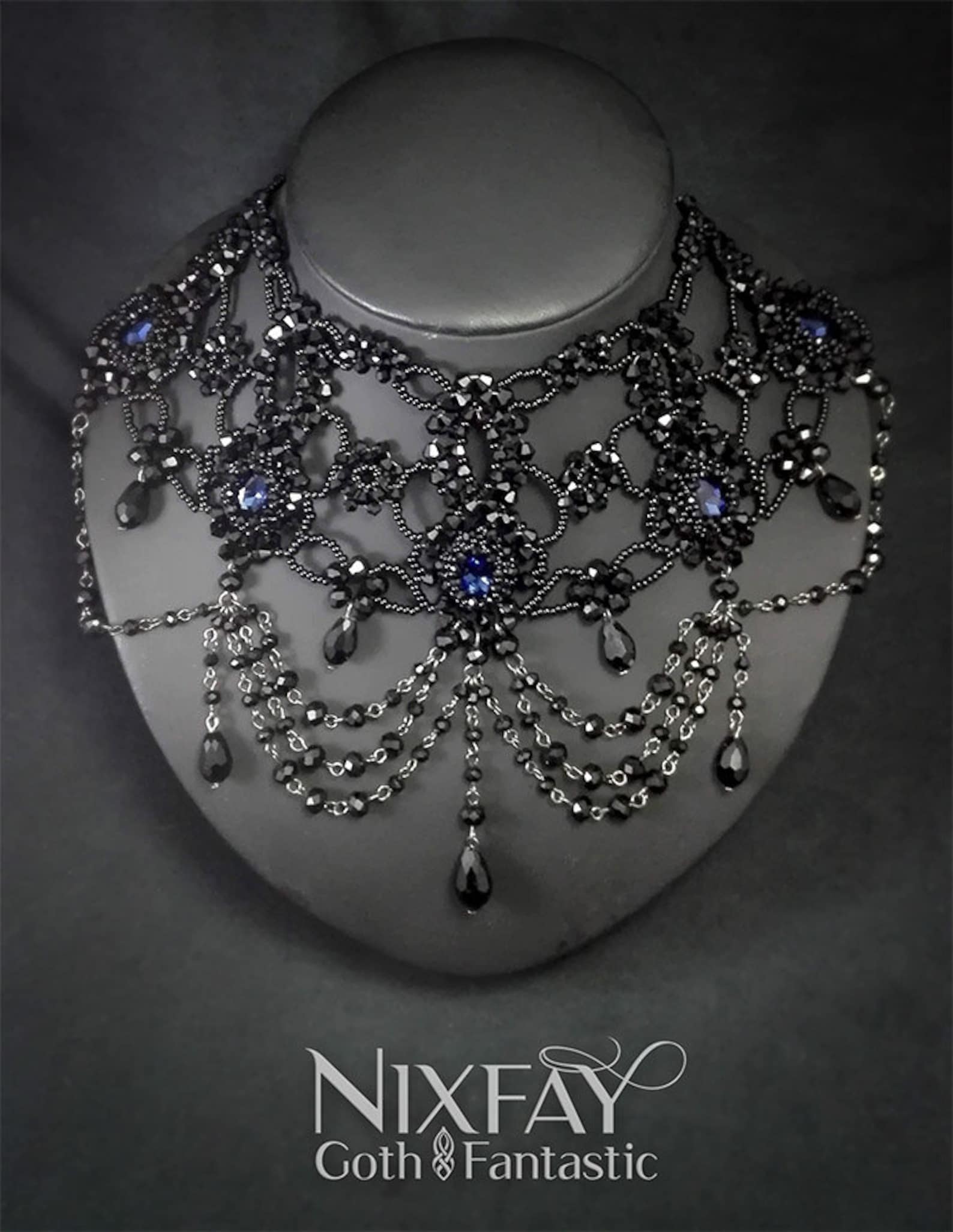 Black beaded gothic choker with sapphire blue rhinestones and layered teardrop chains on velvet display bust.