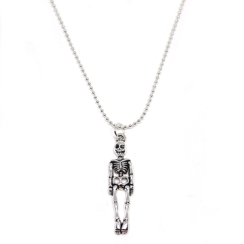 May include: A silver-colored skeleton pendant necklace. The pendant is a detailed miniature skeleton, hanging from a ball chain necklace. The necklace is a simple, yet striking piece of jewelry, perfect for those who appreciate unique and gothic-inspired accessories.