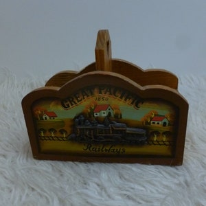 Puede incluir: Porta servilletas de madera con una escena pintada de una locomotora y las palabras "Great Pacific Railways 1850".