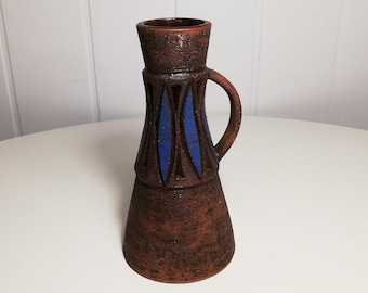 Könnte beinhalten: Eine braune Keramikvase mit einem blauen geometrischen Muster und einem Henkel. Die Vase hat eine strukturierte Oberfläche und eine leicht ausgestellte Öffnung.