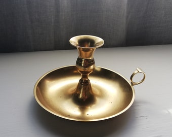 May include: A gold metal candle holder with a round base and a handle. The holder has a decorative design and is perfect for holding a candle.