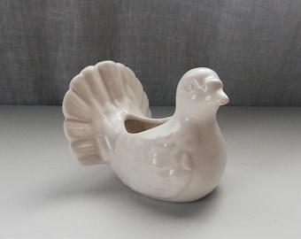 May include: White ceramic dove planter with a detailed tail feather design. The planter has a small opening on the top for planting.