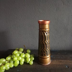 Puede incluir: Un jarrón de cerámica marrón y cobre con un patrón geométrico. El jarrón tiene un borde de cobre y una superficie texturizada.