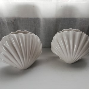 Może przedstawiać: Dwa białe ceramiczne wazony w kształcie muszli. Wazony są gładkie i mają błyszczące wykończenie.